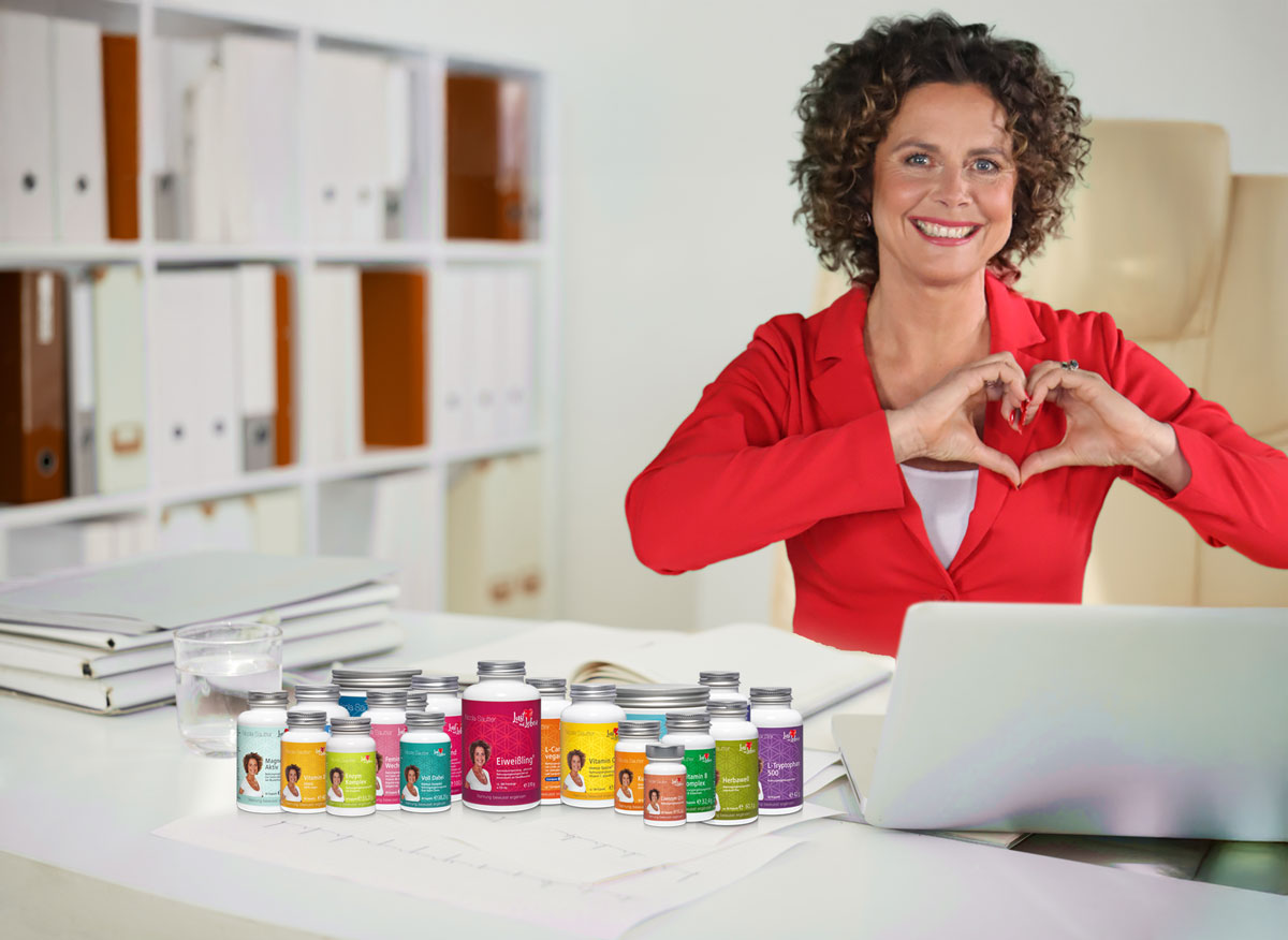 Auf einem weißen Tisch stehen Top-Produkte von Welleat, dahinter steht Nicola Sautter und formt mit den Händen ein Herz